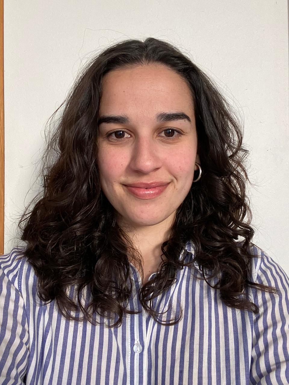Person with curly hair wearing a striped shirt, smiling at the camera against a plain background.