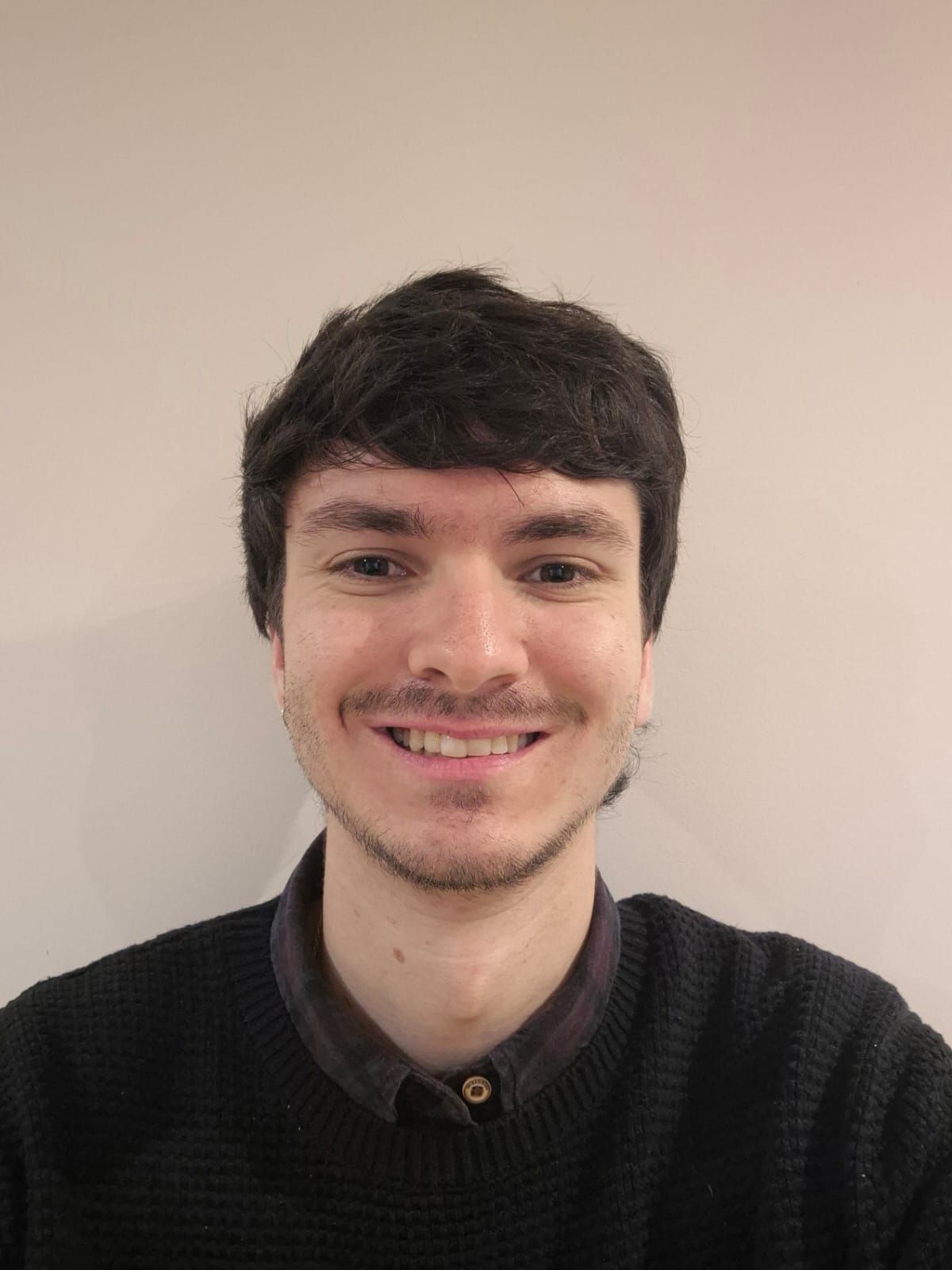 Smiling person with short dark hair wearing a black sweater, posing against a plain background.
